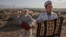 Uyghur men fold up their prayer rugs after praying at the grave of a loved one 