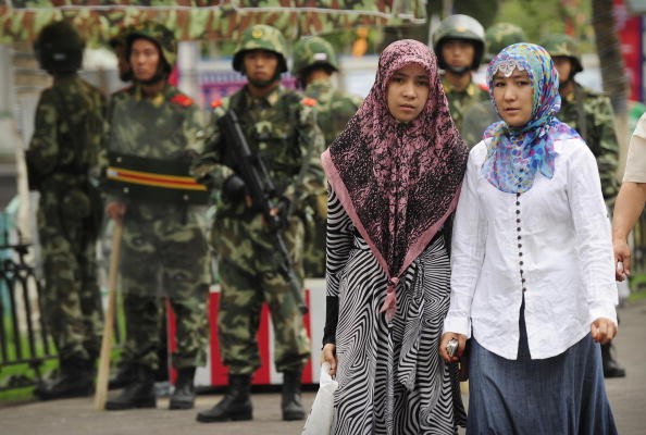 Ethnic Uighur women pass near armed Chinese policemen