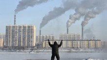 An elderly man exercises in the morning as he faces chimneys emitting smoke behind buildings across the Songhua river in Jilin, Jilin province, China