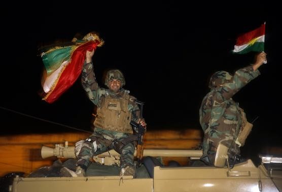 Iraqi Kurdish peshmerga fighters wave Kurdish flags atop an army vehicle as they move towards the Syrian town of Kobani from the border town of Suruc, Sanliurfa province, October 31, 2014. 