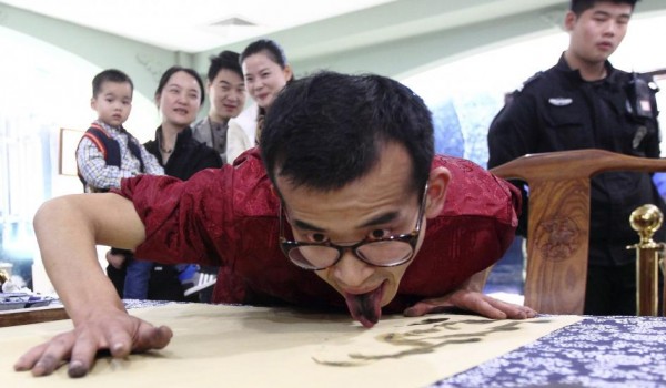 People look on as folk artist Han Xiaoming demonstrates painting with his tongue, in Hangzhou, Zhejiang province November 9, 2014. Han dipped his tongue into ink and then painted on the paper, he also did final adjustments of the painting with his fingers