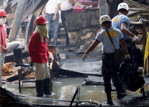Workers look as police carry a body bag containing the charred remains of a worker inside the gutted slipper factory in Valenzuela, Philippines May 14, 2015