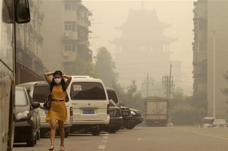 A woman wears a mask as she walks along a street in front of a Chinese temple during a hazy day in Wuhan, Hubei province June 11, 2012. 