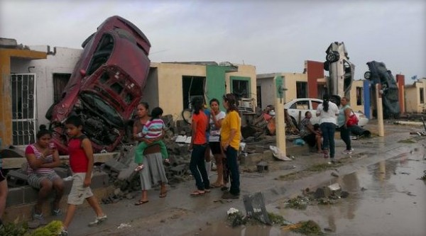 Residents stand outside their homes as damaged cars are seen after a tornado hit the town of Ciudad Acuna