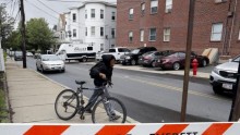 A local youth wheels his bicycle past law enforcement officials gathered on a residential street in Everett, Massachusetts June 2, 2015.