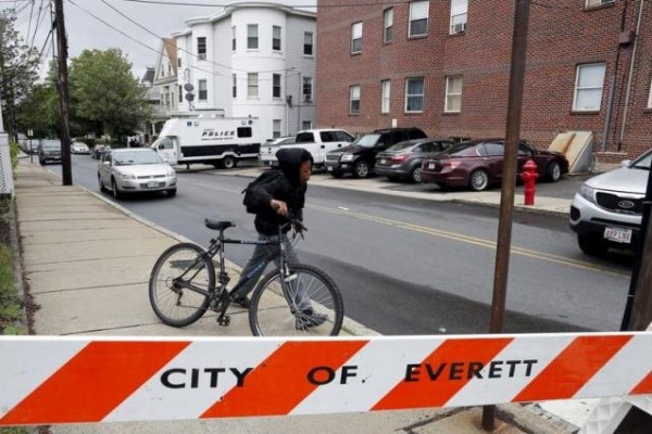 A local youth wheels his bicycle past law enforcement officials gathered on a residential street in Everett, Massachusetts June 2, 2015.