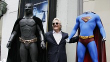Film producer Jon Peters poses with costumes of Batman (left) and Superman.