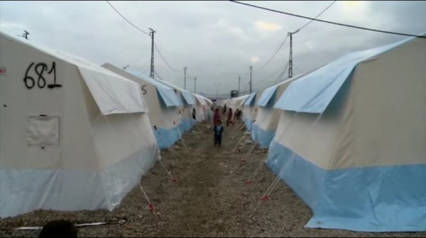 A refugee camp in Europe is shown with kids strolling in the aisle of tents.