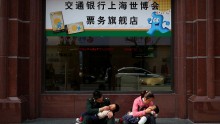 Parents hold children as they sit outside a ticket store for the World Expo 2010