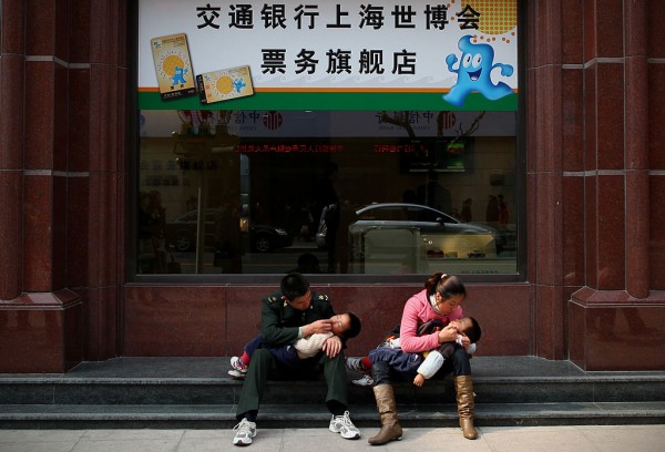 Parents hold children as they sit outside a ticket store for the World Expo 2010