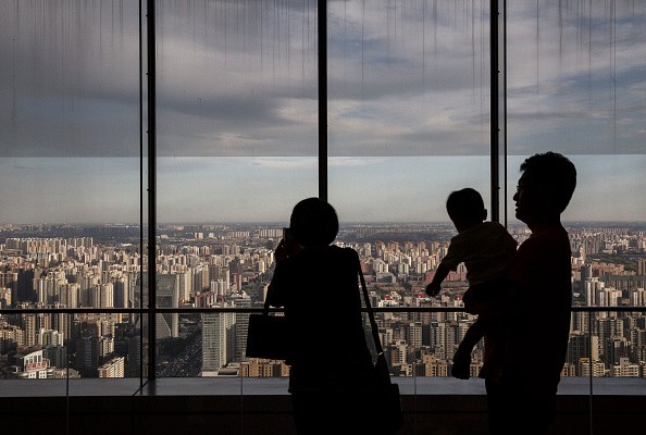 A Chinese couple hold stand with their child as they look out on residential and office buildings from a luxury hotel 