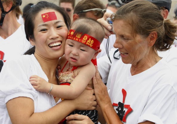 A Greek member of a bicycle team (R) talks with a mother and her child on the Tiananmen Square on Aug. 6, 2008 in Beijing, China. Female employees in Beijing now enjoy longer maternity leave. (Photo: China Photos/Getty Images)