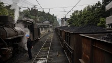 A railway worker stands by as a train carrying coal passes by next a coal powered steam engine in the workshop on March 27, 2015 at a station in the town of Shixi , Sichuan Province, in Southern China. (Photo: Kevin Frayer/Getty Images)