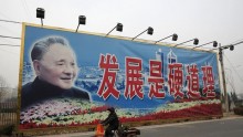 A woman rides a tricycle past a giant poster of late Chinese leader Deng Xiaoping in Beijing.