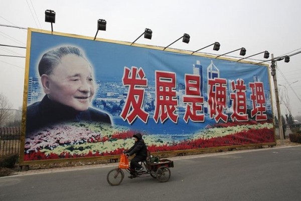 A woman rides a tricycle past a giant poster of late Chinese leader Deng Xiaoping in Beijing.