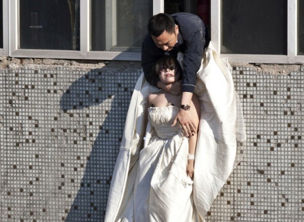 A 22-year-old woman in a wedding gown is grabbed by Guo Zhongfan, a local community officer, as she attempts to kill herself by jumping out of a seven-storey residential building in Changchun, China in 2011.
