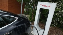 A Tesla electric-powered sedan stands at a Tesla charging station at a highway rest-stop