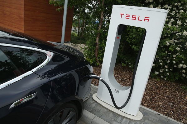 A Tesla electric-powered sedan stands at a Tesla charging station at a highway rest-stop