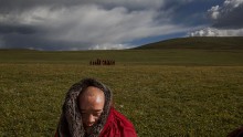 A Tibetan Buddhist monk sits on the grasslands outside a monastery next to a government resettlement community for former nomads at Tibetan Plateau in Yushu County, Qinghai, China
