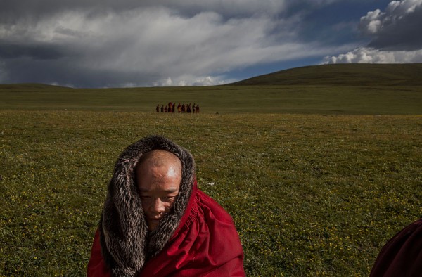 A Tibetan Buddhist monk sits on the grasslands outside a monastery next to a government resettlement community for former nomads at Tibetan Plateau in Yushu County, Qinghai, China