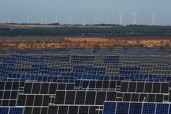 Photovoltaic power panels stand at Abaste's El Bonillo Solar Plant while wind turbines spin at a wind farm on the background on December 2, 2015 in El Bonillo, Albacete province, Spain. 